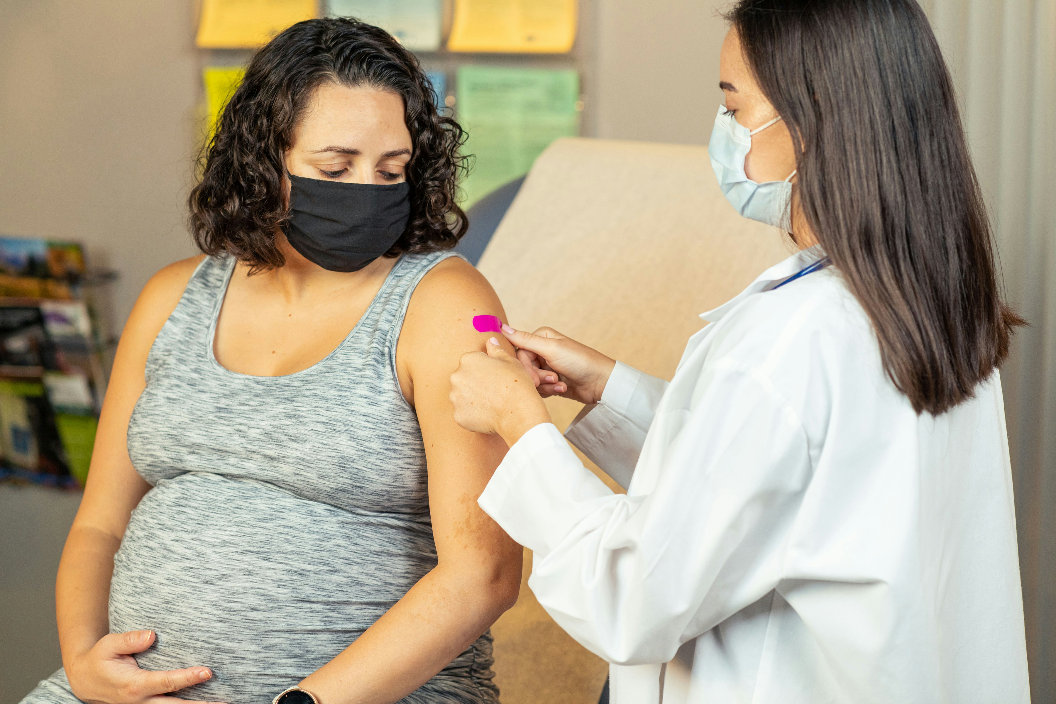 A pregnant woman receives a vaccine at a healthcare facility, with a medical professional.